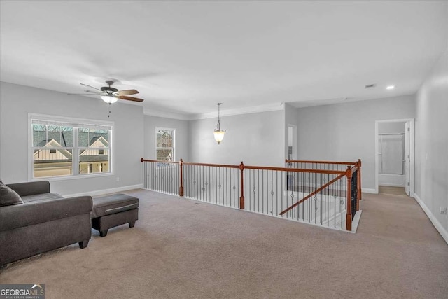 living area with a ceiling fan, carpet, baseboards, crown molding, and an upstairs landing