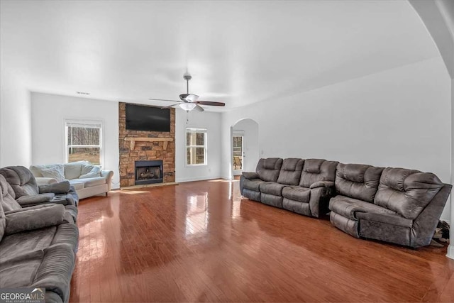 living room featuring a fireplace, wood finished floors, arched walkways, and ceiling fan