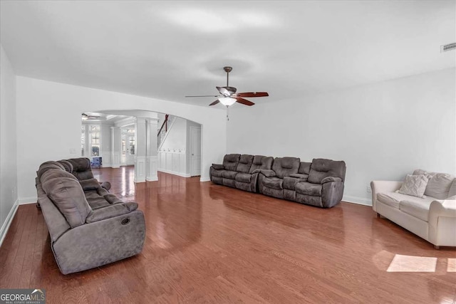 living area featuring wood finished floors, baseboards, decorative columns, arched walkways, and ceiling fan