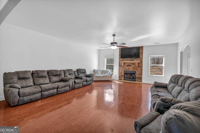 living room featuring arched walkways, a fireplace, ceiling fan, and wood finished floors