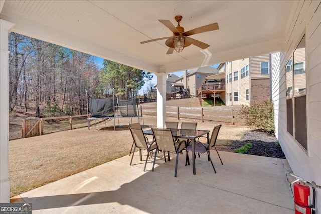 view of patio with outdoor dining area, a trampoline, a ceiling fan, and a fenced backyard