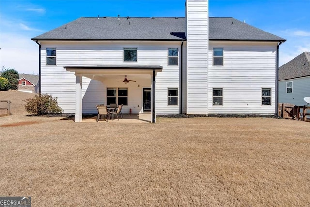 back of house featuring a lawn, a ceiling fan, a patio, a shingled roof, and a chimney