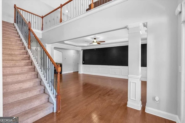 stairs with decorative columns, wood finished floors, a high ceiling, and ceiling fan