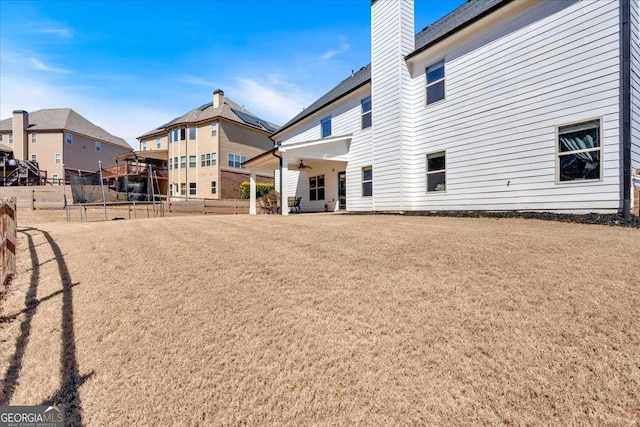 back of property with a chimney, ceiling fan, and fence