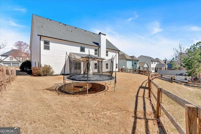 back of house with a residential view, a trampoline, and fence