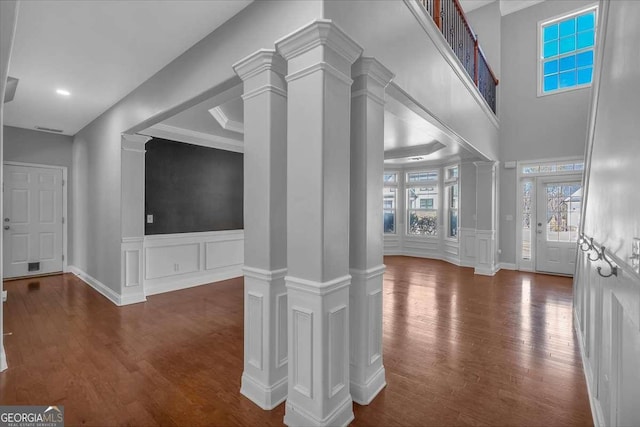 entryway with a decorative wall, a wainscoted wall, ornate columns, and wood finished floors