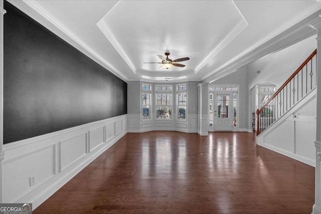 interior space featuring a tray ceiling, decorative columns, wood finished floors, a decorative wall, and a ceiling fan