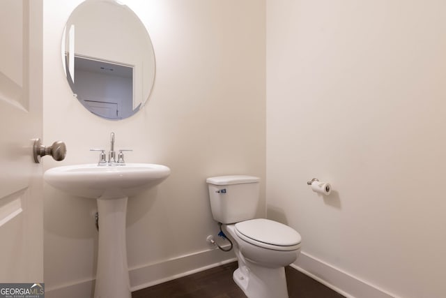 half bathroom with baseboards, toilet, and wood finished floors