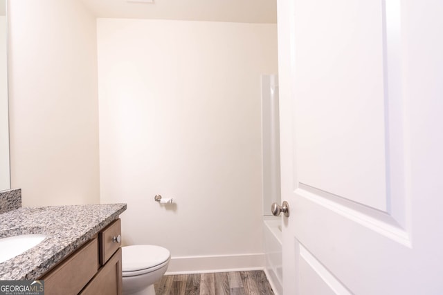 bathroom featuring toilet, wood finished floors, baseboards, a bath, and vanity