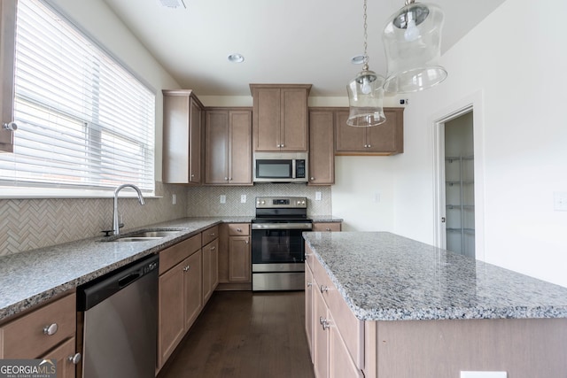 kitchen with light stone countertops, a kitchen island, a sink, stainless steel appliances, and tasteful backsplash