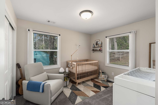 carpeted bedroom featuring a crib, multiple windows, baseboards, and visible vents