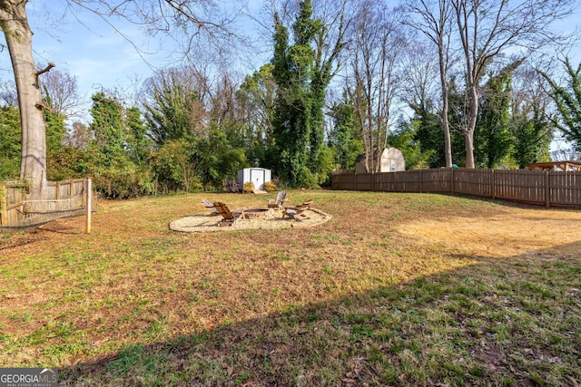 view of yard featuring an outdoor structure, a fenced backyard, a shed, and an outdoor fire pit