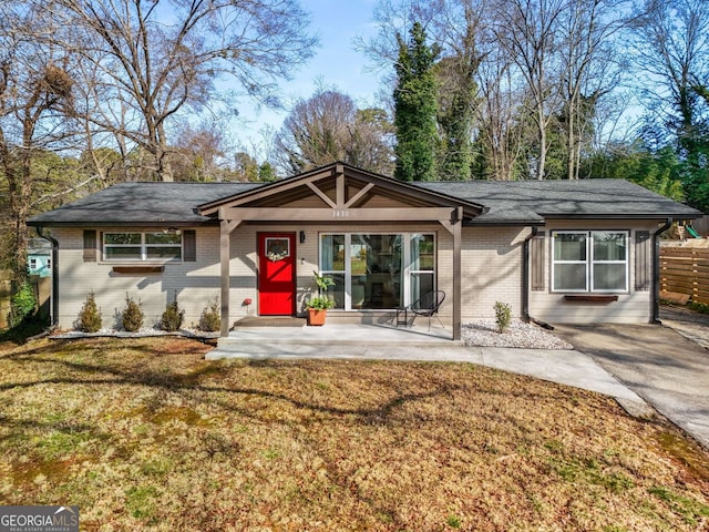 single story home with a front yard, fence, roof with shingles, a patio area, and brick siding