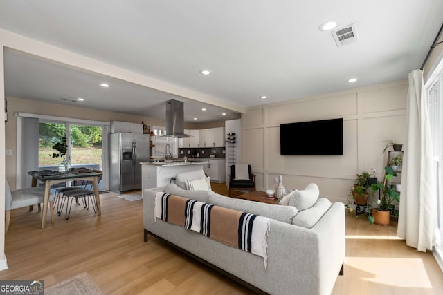 living area with recessed lighting, visible vents, light wood-style flooring, and a decorative wall