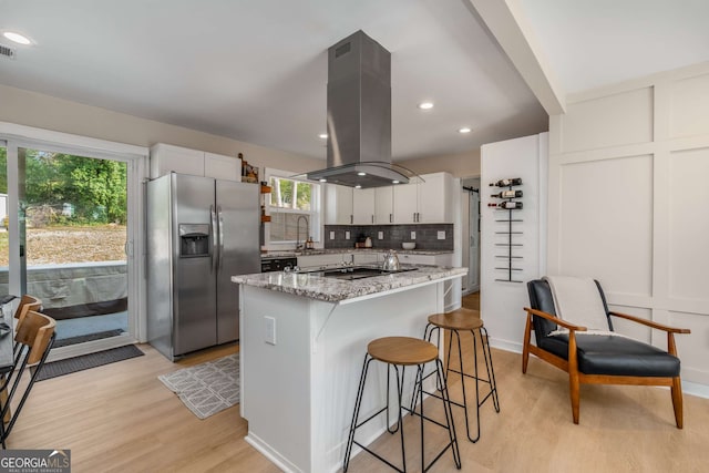 kitchen with light stone counters, backsplash, white cabinets, island range hood, and stainless steel fridge with ice dispenser