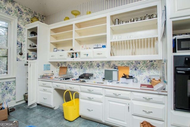 kitchen featuring stainless steel microwave, black oven, wallpapered walls, white cabinetry, and open shelves