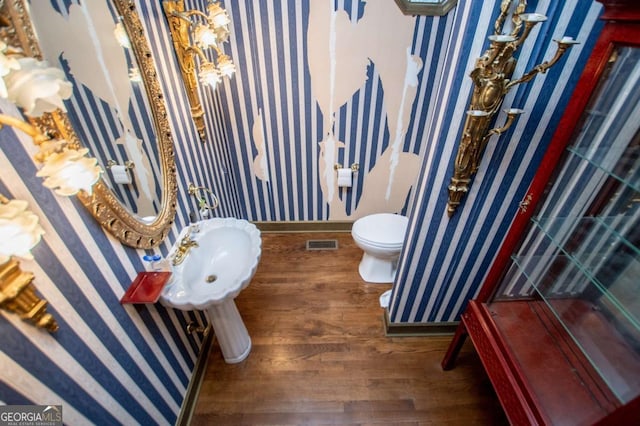 bathroom with wood finished floors, visible vents, baseboards, wallpapered walls, and toilet