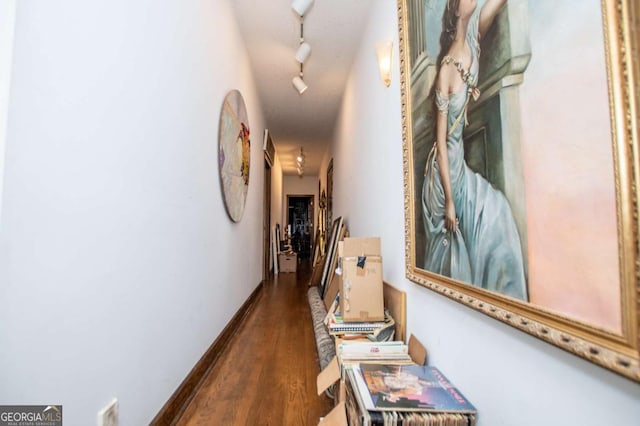 corridor featuring rail lighting, wood finished floors, and baseboards