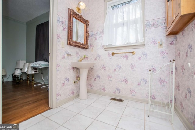 bathroom with visible vents, baseboards, wallpapered walls, ornamental molding, and tile patterned flooring