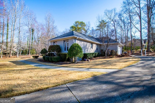 view of property exterior with brick siding, a garage, a lawn, and driveway