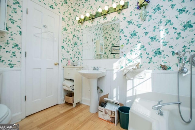 bathroom featuring wallpapered walls, wood finished floors, and wainscoting