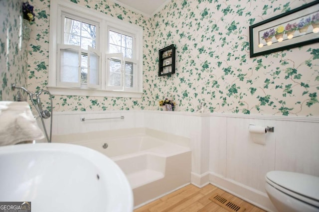 bathroom with wallpapered walls, a garden tub, visible vents, and wainscoting