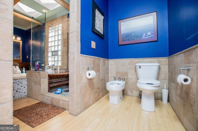 full bathroom with toilet, a bidet, wainscoting, a skylight, and wood finished floors