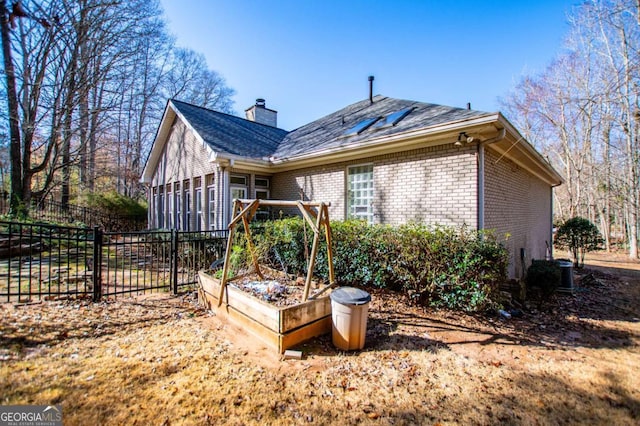 back of house featuring a garden, a chimney, brick siding, and fence