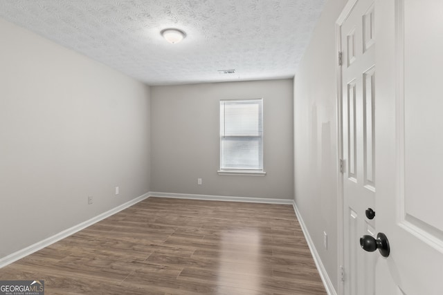 unfurnished room with a textured ceiling, wood finished floors, visible vents, and baseboards