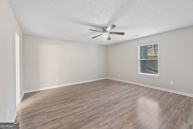 empty room with wood finished floors, a ceiling fan, visible vents, and a textured ceiling