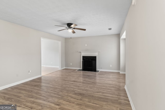 unfurnished living room with baseboards, wood finished floors, ceiling fan, and a fireplace with flush hearth