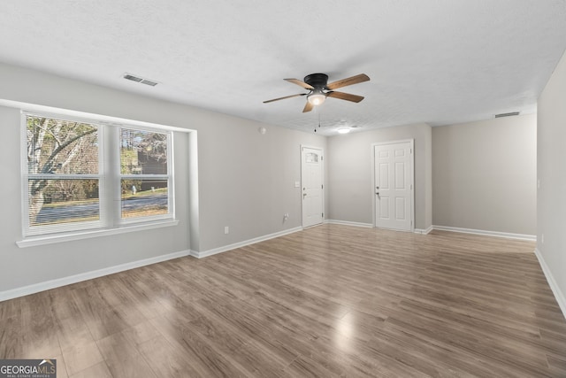 unfurnished living room with visible vents, a textured ceiling, wood finished floors, baseboards, and ceiling fan