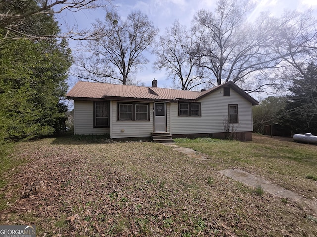 view of front facade featuring a chimney, entry steps, metal roof, and a front lawn