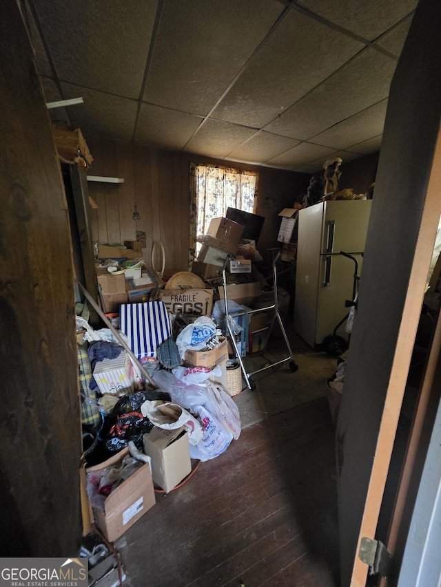 below grade area featuring a drop ceiling, wood walls, freestanding refrigerator, and wood finished floors