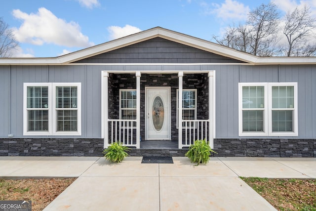 view of exterior entry featuring stone siding and a porch