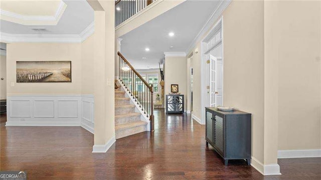 foyer featuring crown molding, stairway, wainscoting, wood finished floors, and a decorative wall