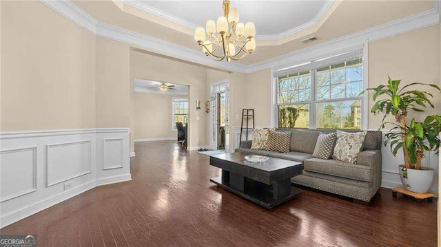 living room featuring a raised ceiling, a notable chandelier, wood finished floors, and crown molding