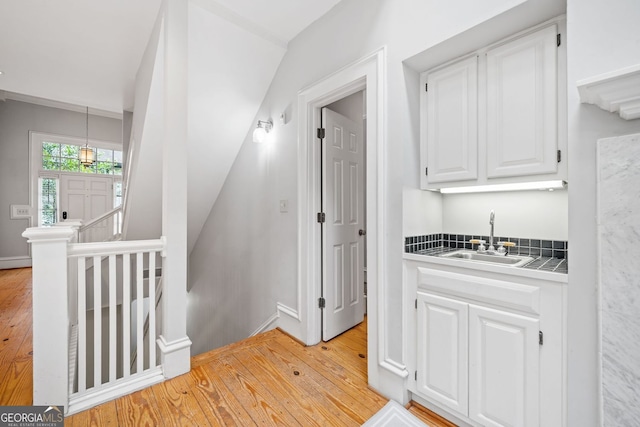 interior space featuring baseboards, an upstairs landing, light wood-type flooring, and a sink