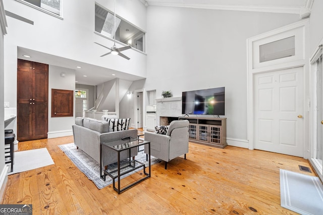 living area with light wood finished floors, visible vents, crown molding, a high ceiling, and a ceiling fan