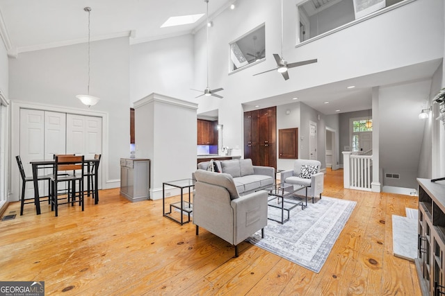 living room featuring light wood finished floors, visible vents, baseboards, a skylight, and a ceiling fan