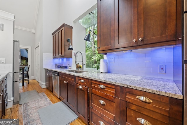 kitchen featuring ornamental molding, a sink, light wood-style floors, appliances with stainless steel finishes, and light stone countertops