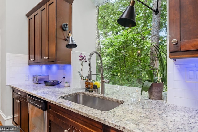 kitchen with a sink, light stone counters, backsplash, and dishwasher