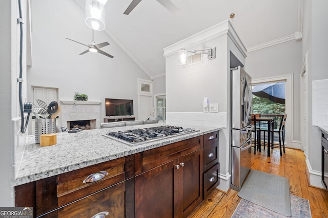 kitchen with light wood finished floors, a fireplace, ceiling fan, ornamental molding, and stainless steel appliances