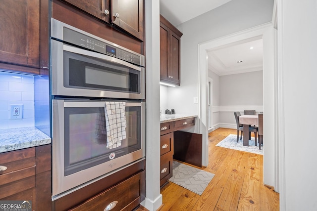 kitchen featuring tasteful backsplash, double oven, crown molding, light wood finished floors, and dark brown cabinets