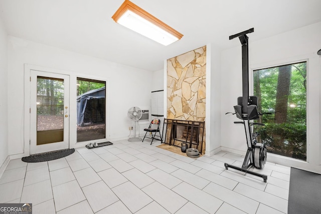 exercise room featuring tile patterned flooring, a stone fireplace, a wall mounted AC, and baseboards