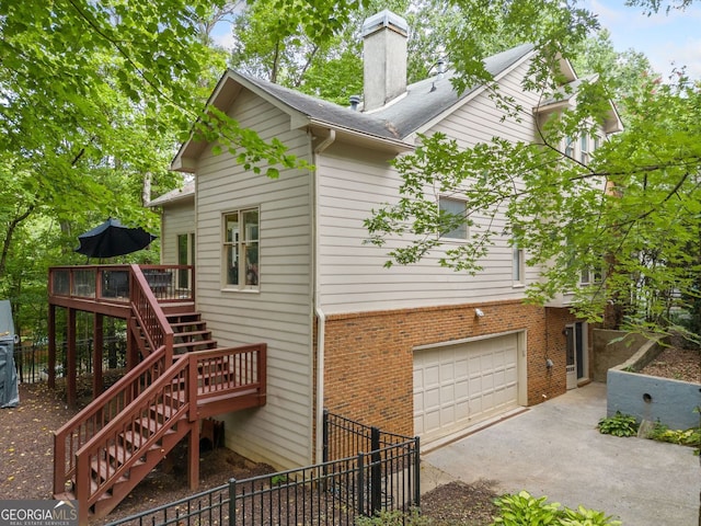 view of side of property with stairway, concrete driveway, an attached garage, brick siding, and a chimney