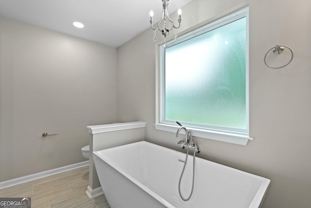 full bathroom with a soaking tub, baseboards, toilet, a chandelier, and wood finished floors