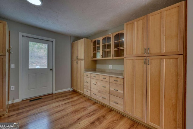 kitchen featuring light brown cabinets, baseboards, light countertops, glass insert cabinets, and light wood-style floors