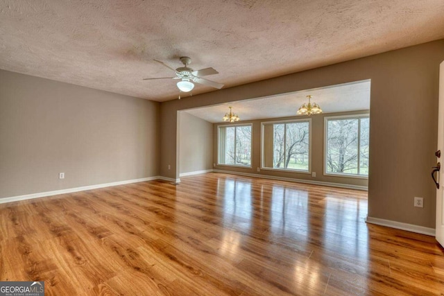 empty room featuring plenty of natural light, ceiling fan with notable chandelier, baseboards, and wood finished floors