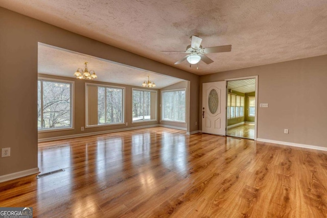 unfurnished living room with light wood finished floors, plenty of natural light, and ceiling fan with notable chandelier
